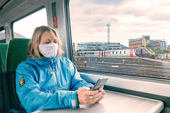 Young lady sat on train with mask (COVID) looking at phone