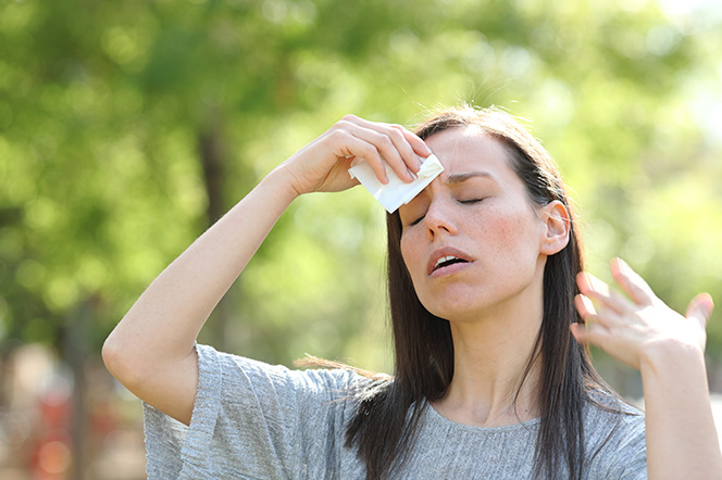 Young woman outside wiping the sweat from her forehead