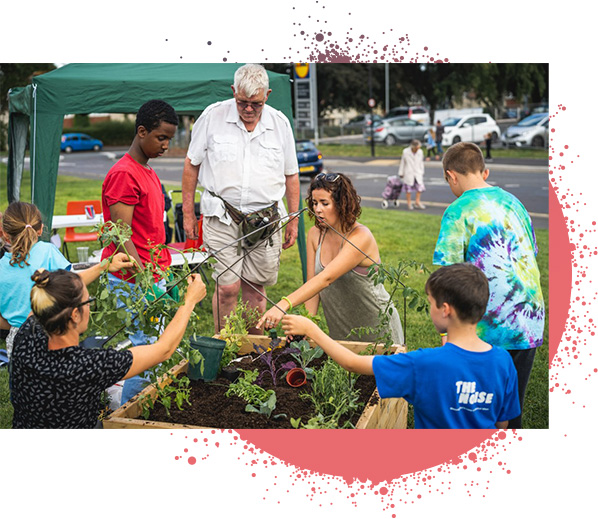 ALW group, adults and children potting plants in large wooden planter.