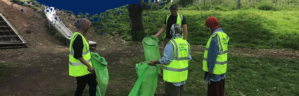 4 people with hi-vis vests litter picking in Bristol park.