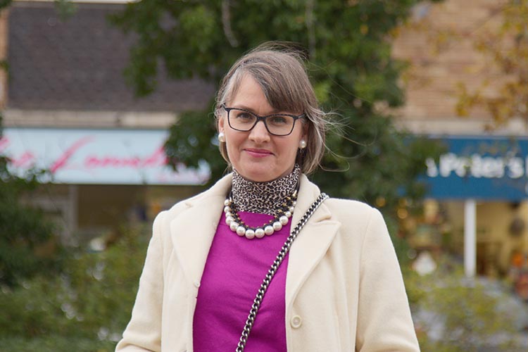 Photo shows woman stood in front of St Peters Hospice shop on a treelined street