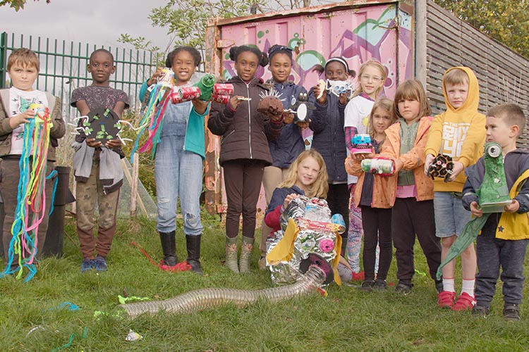 Photo shows a group of 12 children, holding a range of different sculpture pieces made from rubbish
