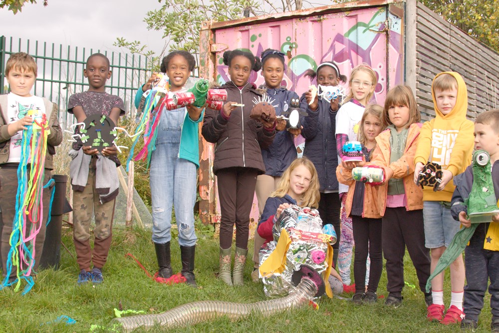 Photo shows a group of 12 children, holding a range of different sculpture pieces made from rubbish